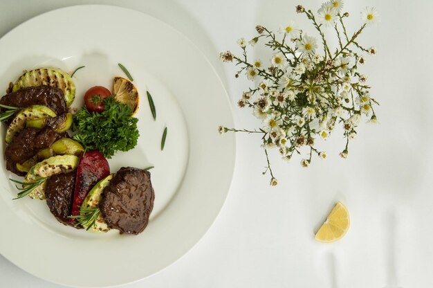 Viande rôtie avec des tranches de citron sur une surface blanche avec une ombre des verres à vin