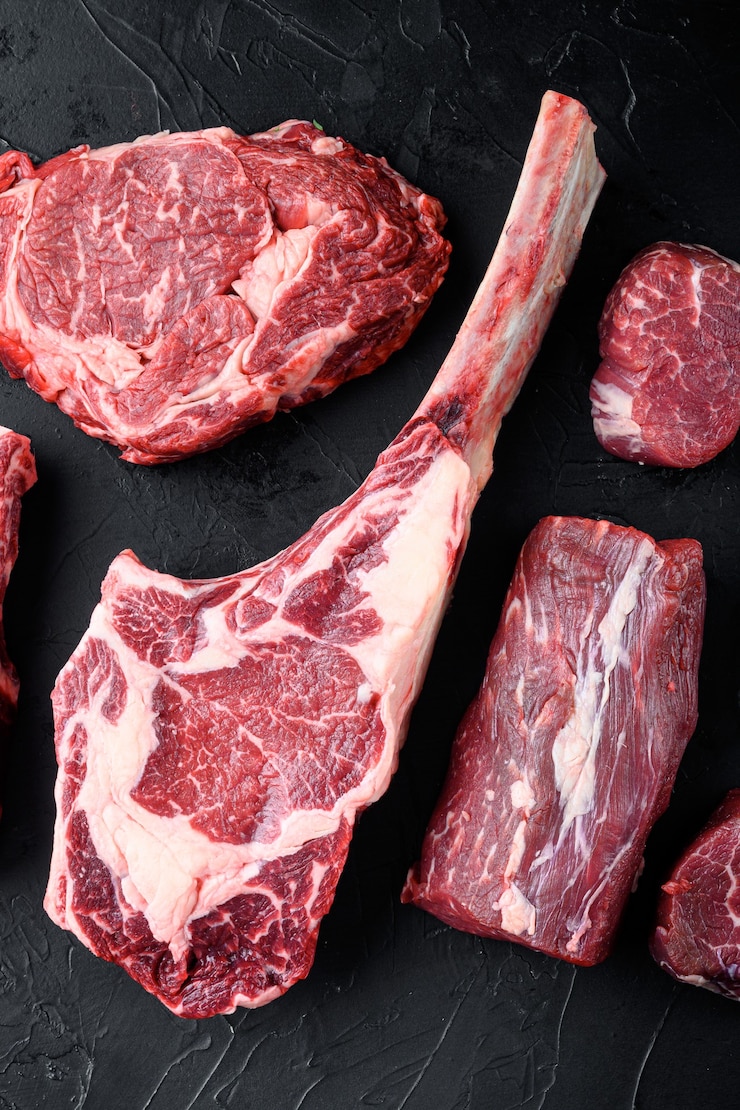 Photo viande rouge de boeuf cru non cuite marbrée d'os dans l'ensemble, sur fond noir en pierre