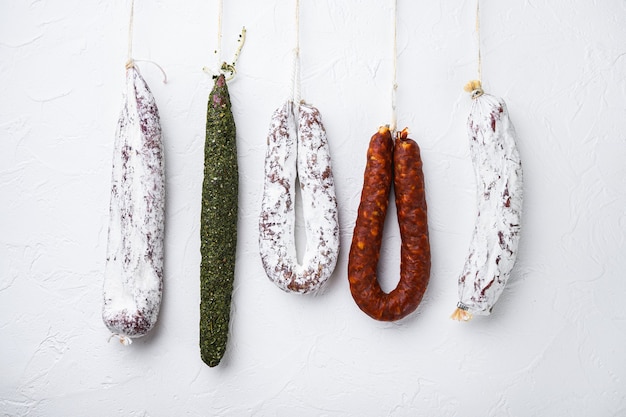 Viande de saucisses séchées traditionnelles suspendues sur fond texturé blanc.