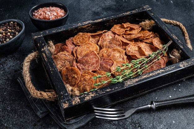 Viande séchée de bœuf et de porc séchée dans un plateau en bois. Fond noir. Vue de dessus.