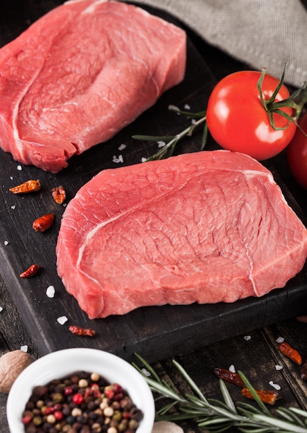 Viande de steak de boeuf cru frais sur une planche de cuisine en bois avec des tomates et du poivre