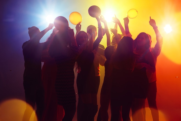 Vibrations. Une foule de personnes en silhouette lève les mains sur la piste de danse sur fond néon. Vie nocturne, club, musique, danse, mouvement, jeunesse. Couleurs jaune-bleu et filles et garçons en mouvement.