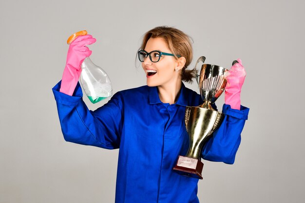 Victoire sur la boue femme heureuse en uniforme et gants tenant un spray nettoyant et une coupe trophée d'or