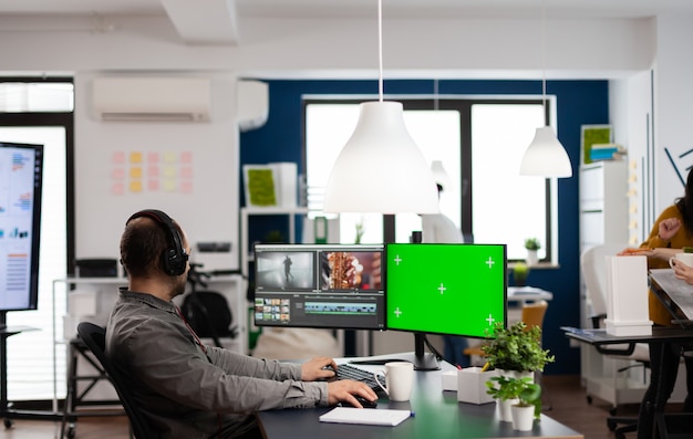 Vidéaste homme avec casque d'édition de film dans un logiciel de post-production travaillant sur écran vert, affichage isolé de la clé chroma de l'ordinateur