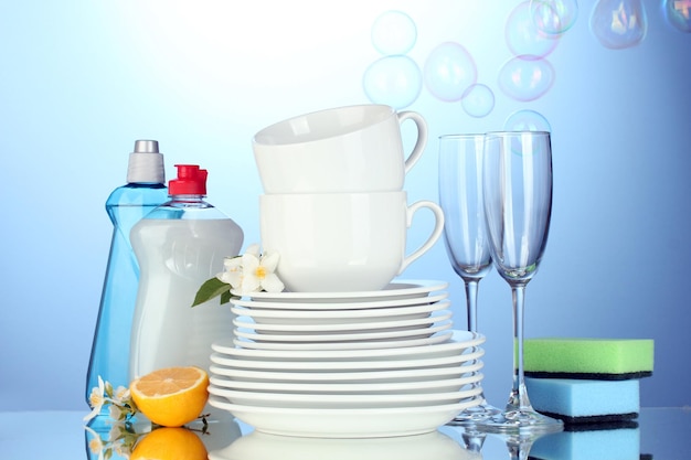 Vider les assiettes propres, les verres et les tasses avec des éponges de liquide vaisselle et du citron sur fond bleu