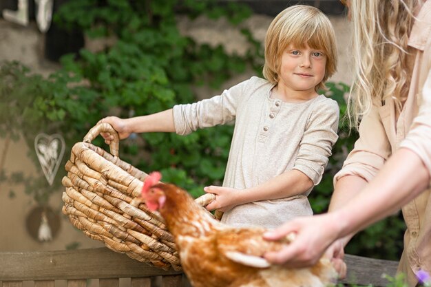 La Vie Du Village. Un Garçon De La Campagne Avec Un Poulet Brun Et Un Grand Panier Dans La Cour