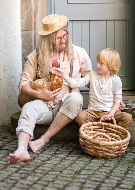 La vie du village. Pays garçon avec papa poulet brun et un grand panier dans la cour près de la porte d'entrée. Jour d'été