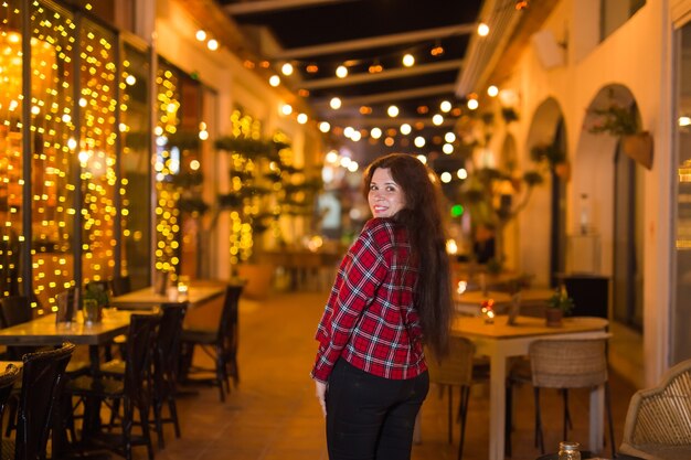 Vie nocturne, gens et concept amusant - Belle jeune femme pose près d'un restaurant lumineux dans la rue pendant la nuit.