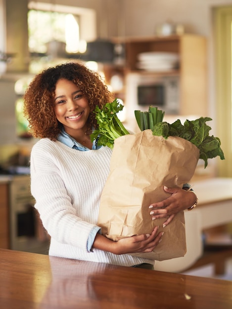 Une vie saine commence à la maison Portrait d'une jeune femme heureuse tenant un sac plein de légumes sains à la maison