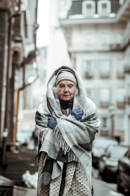 La vie des sans-abri. Triste femme sérieuse fermant les yeux tout en étant recouverte de plaid