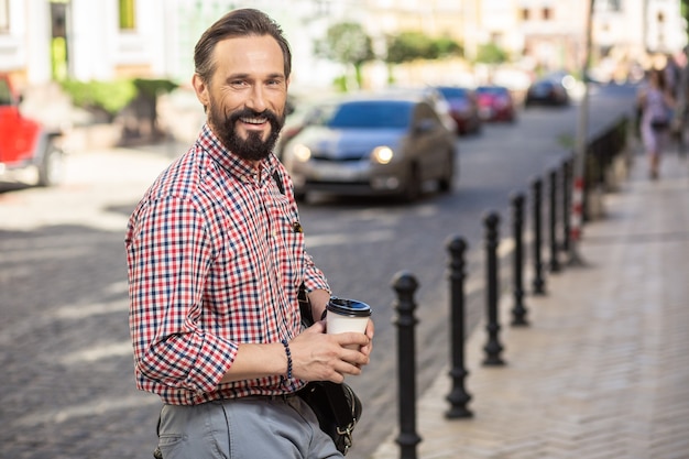 La vie en ville. Cheerful handsome male manager marchant au travail tout en buvant du café