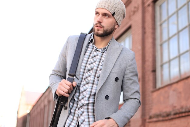 La vie en ville. Jeune homme élégant en manteau gris et chapeau marchant dans la rue de la ville.