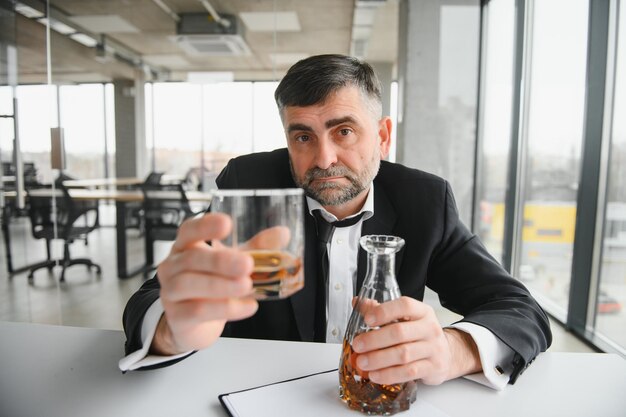 Le vieil homme d'affaires boit de l'alcool au bureau.