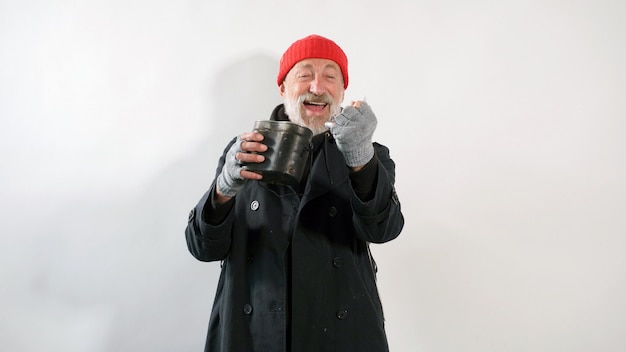 Un vieil homme âgé, un mendiant, un sans-abri avec une barbe grise sourit tenant des dollars dans sa main sur un mur blanc isolé