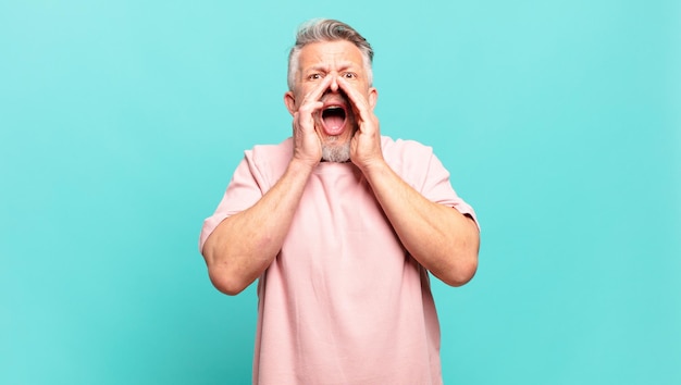 Vieil homme âgé se sentant heureux, excité et positif, donnant un grand cri avec les mains à côté de la bouche, appelant