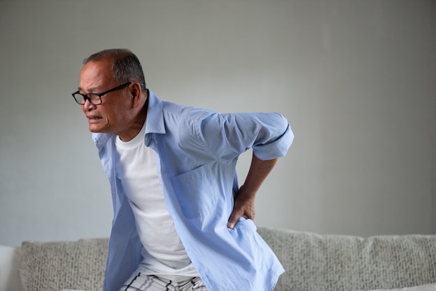 Photo vieil homme asiatique assis sur un canapé et ayant des maux de dos