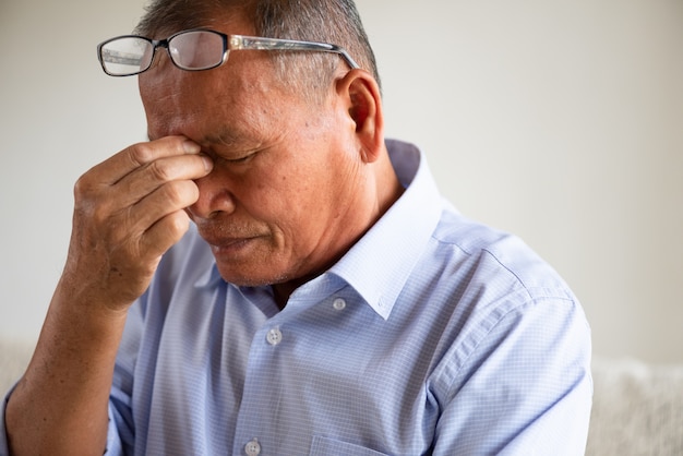 Vieil homme assis sur un canapé et ayant des maux de tête à la maison. Concept de soins de santé senior.