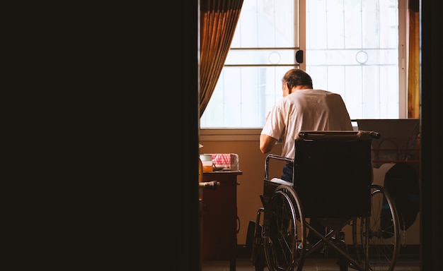 Vieil homme assis seul dans un fauteuil roulant à la maison