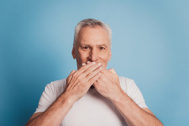 Un vieil homme aux cheveux gris choqué couvre la bouche avec les mains isolées sur fond bleu studio