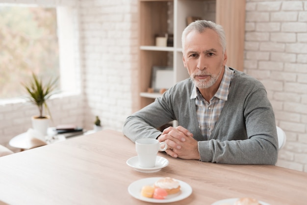 Vieil homme aux cheveux gris est assis à table boire du café