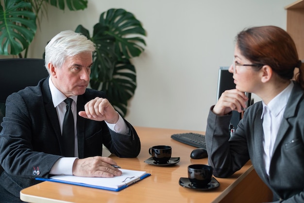 Un vieil homme aux cheveux gris interroge une jeune femme aux cheveux roux Un vieux patron masculin embauche une employée Discussion de deux collègues