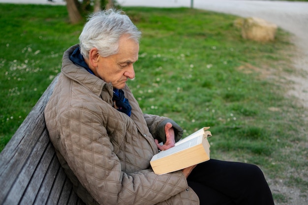 Vieil homme aux cheveux gris lisant un livre assis sur un banc