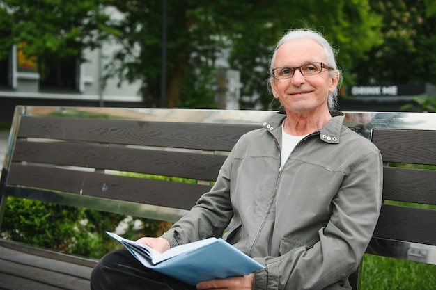 Vieil homme aux cheveux gris lit un livre sur un banc dans le parc Repos dans le parc