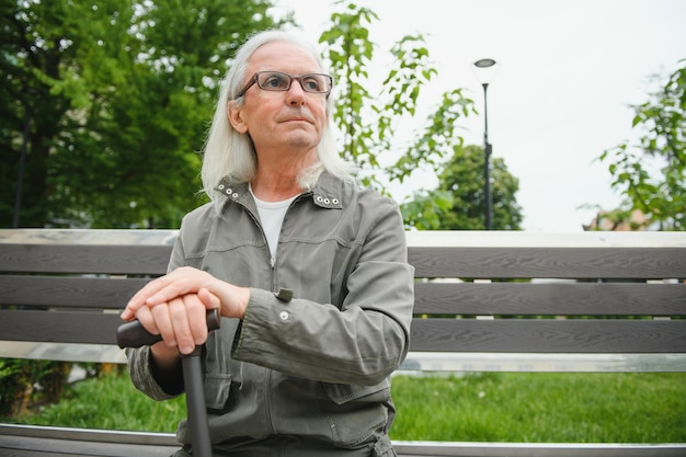 Le vieil homme aux cheveux gris se repose sur le banc dans le parc d'été