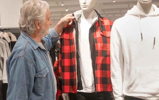 Le vieil homme à la barbe et aux cheveux blancs regarde les objets exposés sur le mannequin