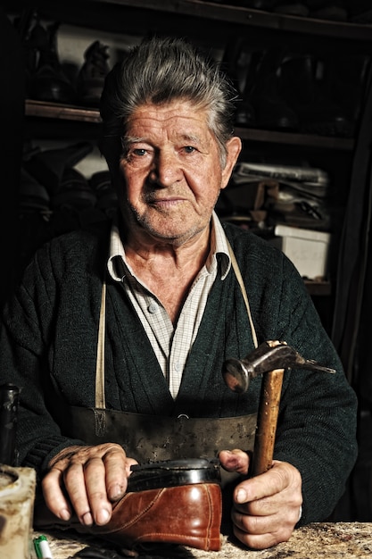 Vieil homme, cordonnier, réparant une vieille chaussure à la main dans son atelier