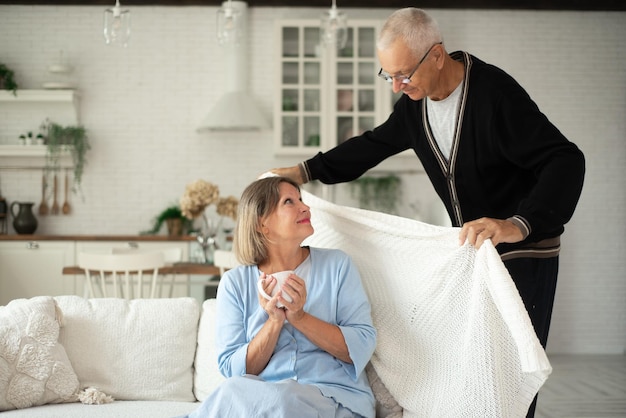 Un vieil homme couvre sa femme avec une couverture chaude pour se réchauffer en hiver