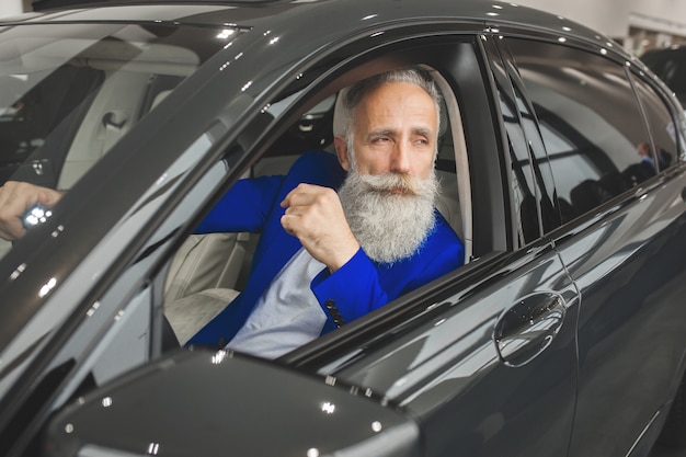 Vieil homme élégant dans la voiture de luxe. Homme avec barbe et mustash au volant d'une automobile. salon de vente de voitures.