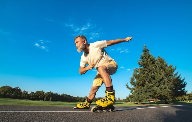 Le vieil homme faisant du patin à roues alignées sur la route