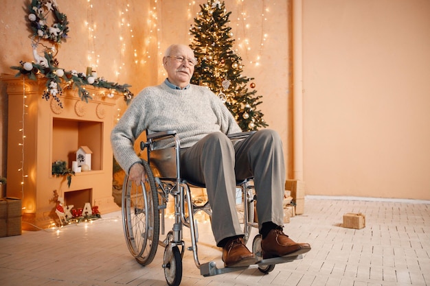 Vieil homme sur un fauteuil roulant assis près de l'arbre de Noël seul