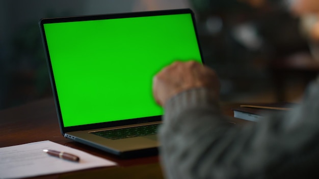 Photo un vieil homme inconnu effectuant un appel vidéo sur un ordinateur portable à écran vert à la maison un homme âgé non reconnaissable parlant en ligne à un ordinateur de mock-up une personne masculine effectuant une conférence en ligne à la maison