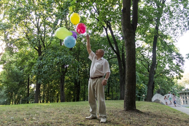 Un vieil homme joue dans le parc avec des ballons lumineux le jour de son anniversaire