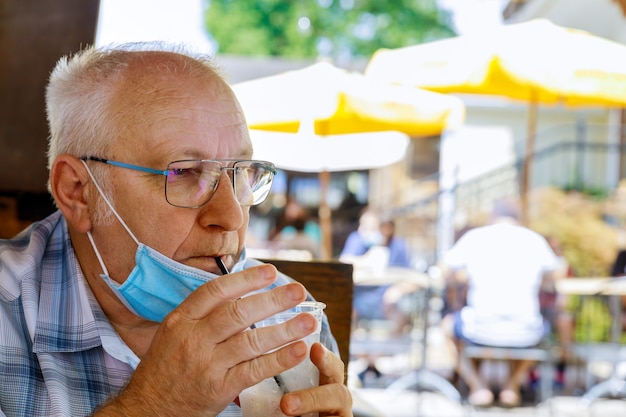 Vieil homme en masque facial médical est une eau de boisson