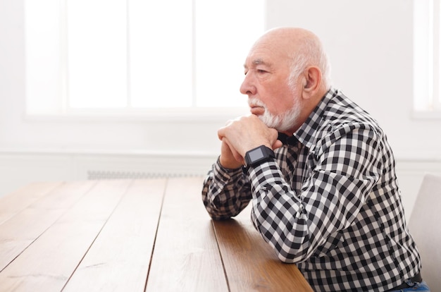 Un vieil homme pensif assis à une table en bois, copiez l'espace. Homme senior sérieux avec une expression faciale réfléchie