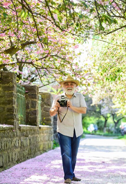 Un vieil homme regarde un photographe de jeunes plantes homme prendre une photo de fleur de sakura Photographe de jardin en fleurs de cerisier prenant une photo d'abricot fleurit au printemps avec une fleur rose Été chaud