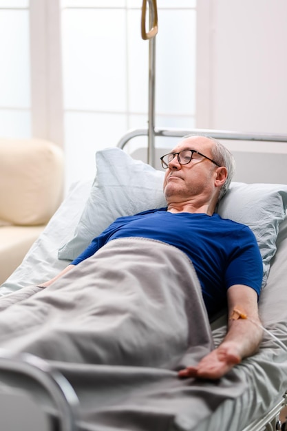 Photo vieil homme à la retraite dans une maison de soins infirmiers allongé sur le lit avec une transfusion attachée à son bras