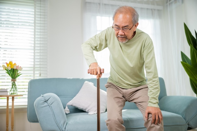 Vieil homme senior asiatique avec des lunettes de type à se lever du canapé avec un bâton de canne de marche