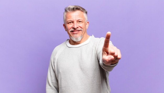 Vieil homme senior souriant fièrement et avec confiance faisant triomphalement la pose numéro un, se sentant comme un leader