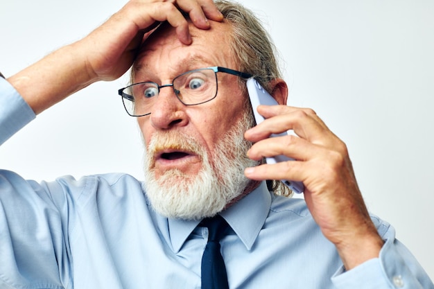 Vieil homme avec téléphone choqué en studio sur fond blanc