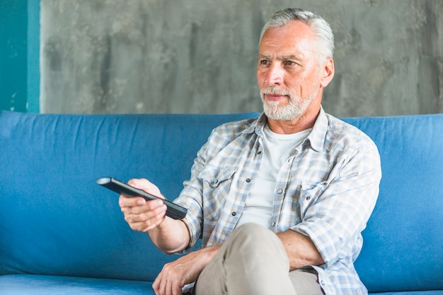 Vieil homme tenant la télécommande en regardant la télévision