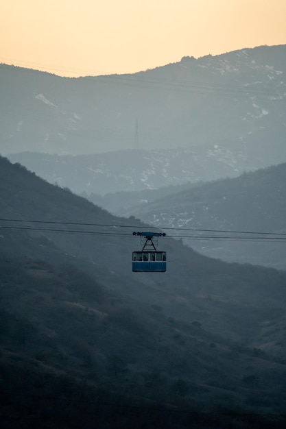 La vieille cabine bleue du téléphérique se déplace sur fond de montagnes à crête dans le brouillard Photo couleur pastels