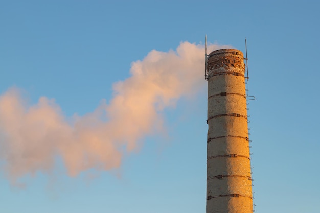 une vieille cheminée en brique d'une chaufferie d'usine avec de la fumée sur un fond de ciel bleu