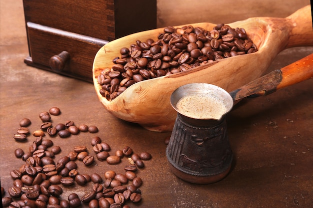 Vieille cuillère en bois avec grains de café, moulin à café et Cezve sur une table en pierre sombre.