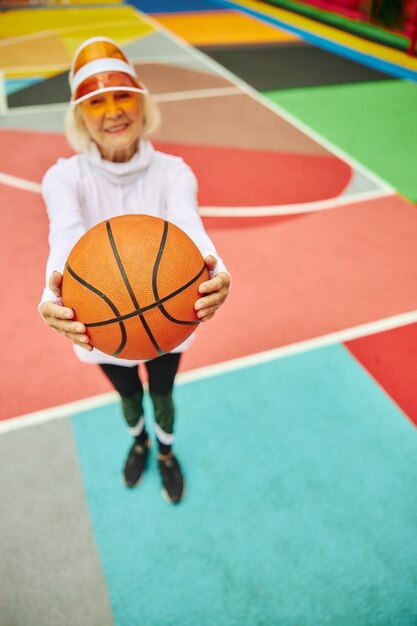 Vieille dame en bonne santé et joyeuse avec ballon de basket sur une place colorée à l'extérieur