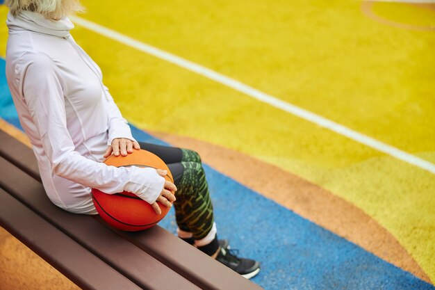 Vieille dame en bonne santé et joyeuse avec ballon de basket sur une place colorée à l'extérieur