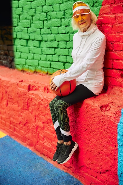 Vieille dame en bonne santé et joyeuse avec ballon de basket sur une place colorée à l'extérieur